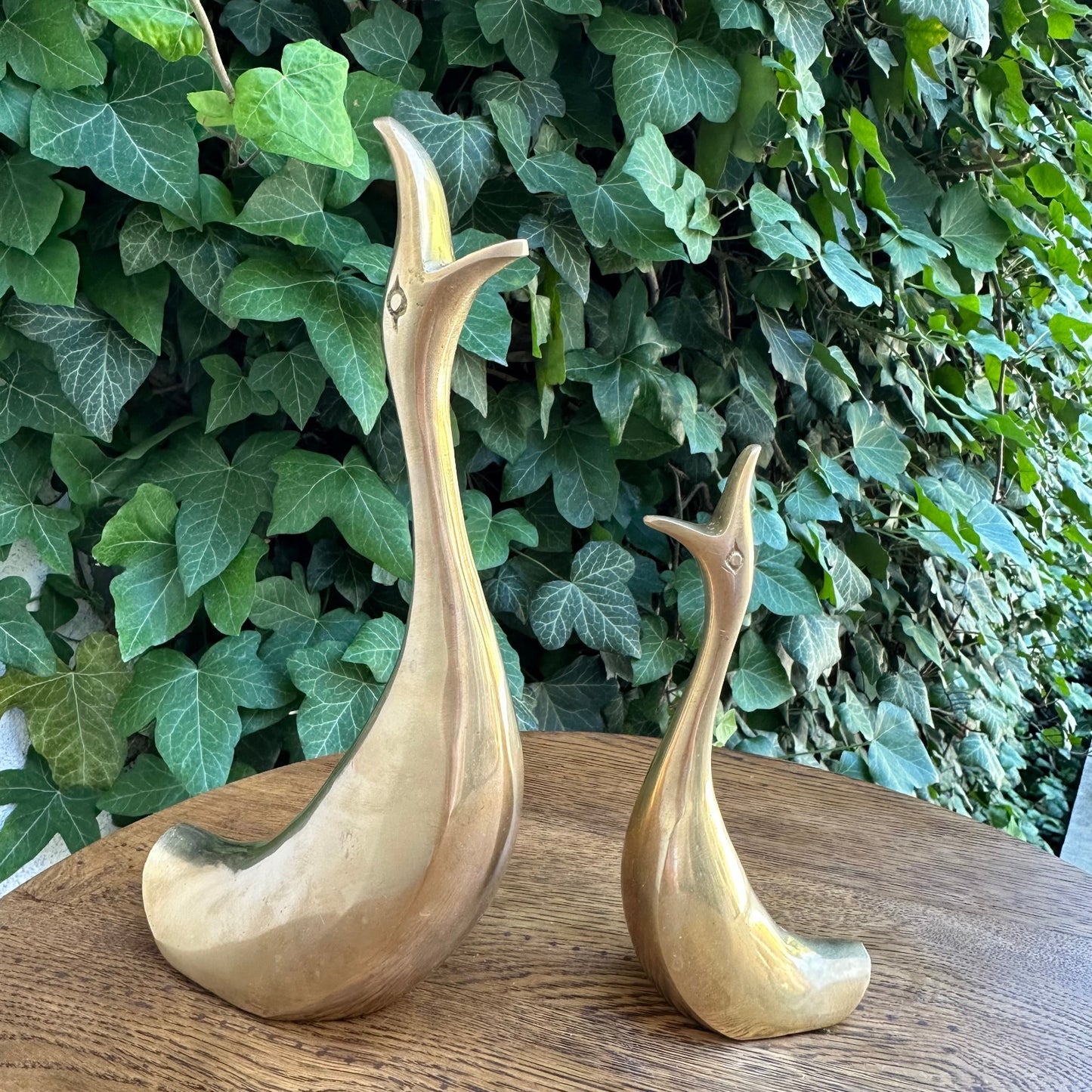Two gold bird sculptures on a wooden surface with a green leafy background