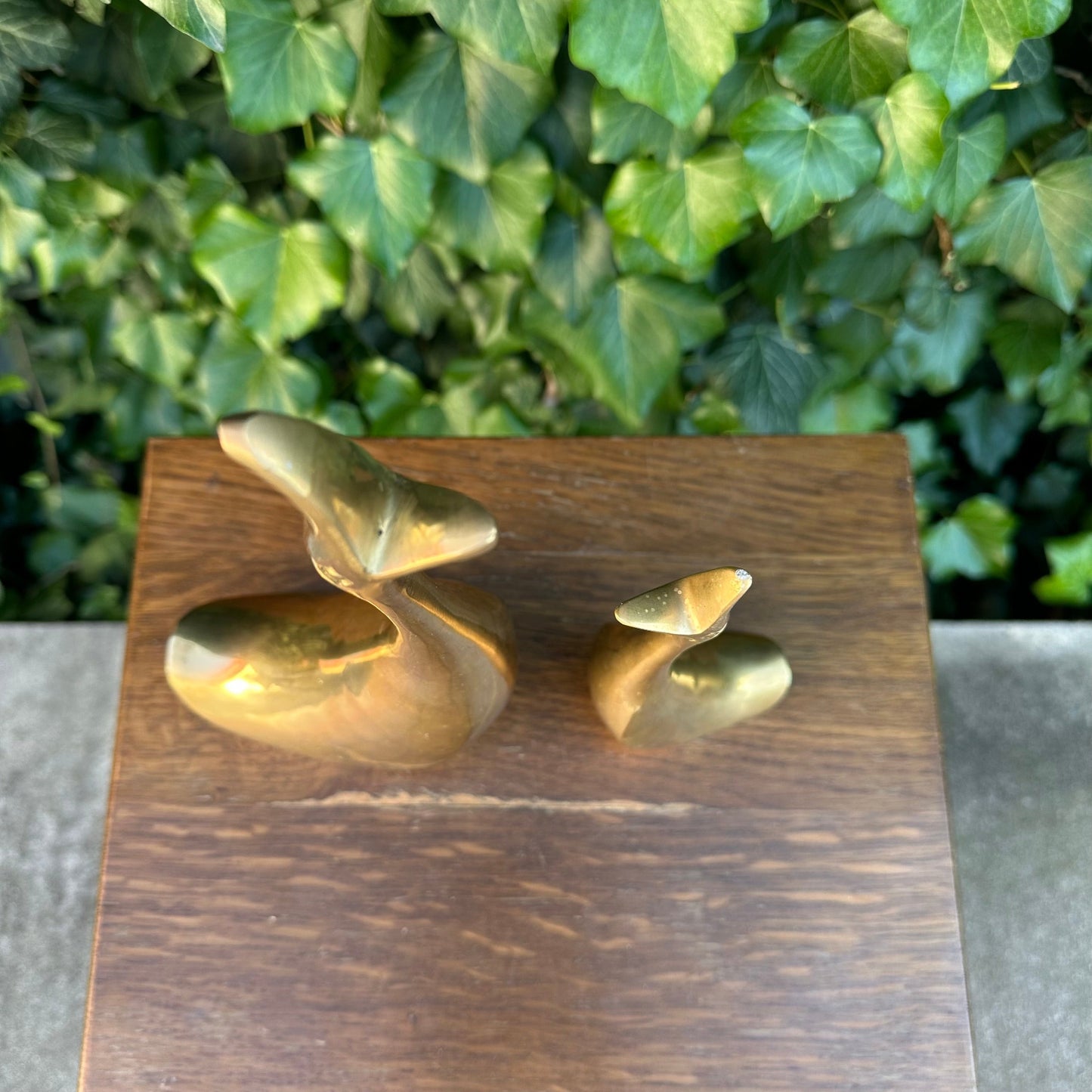 Gold abstract sculpture on a wooden stand with green foliage in the background