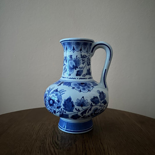 Blue and white floral-patterned ceramic pitcher on a wooden surface with a plain background