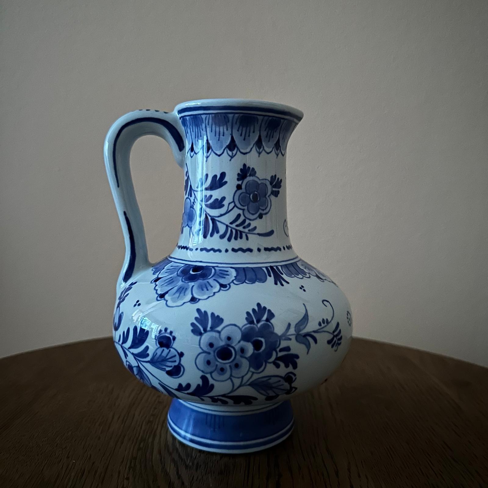 Blue and white floral-patterned ceramic pitcher on a wooden surface with a beige background