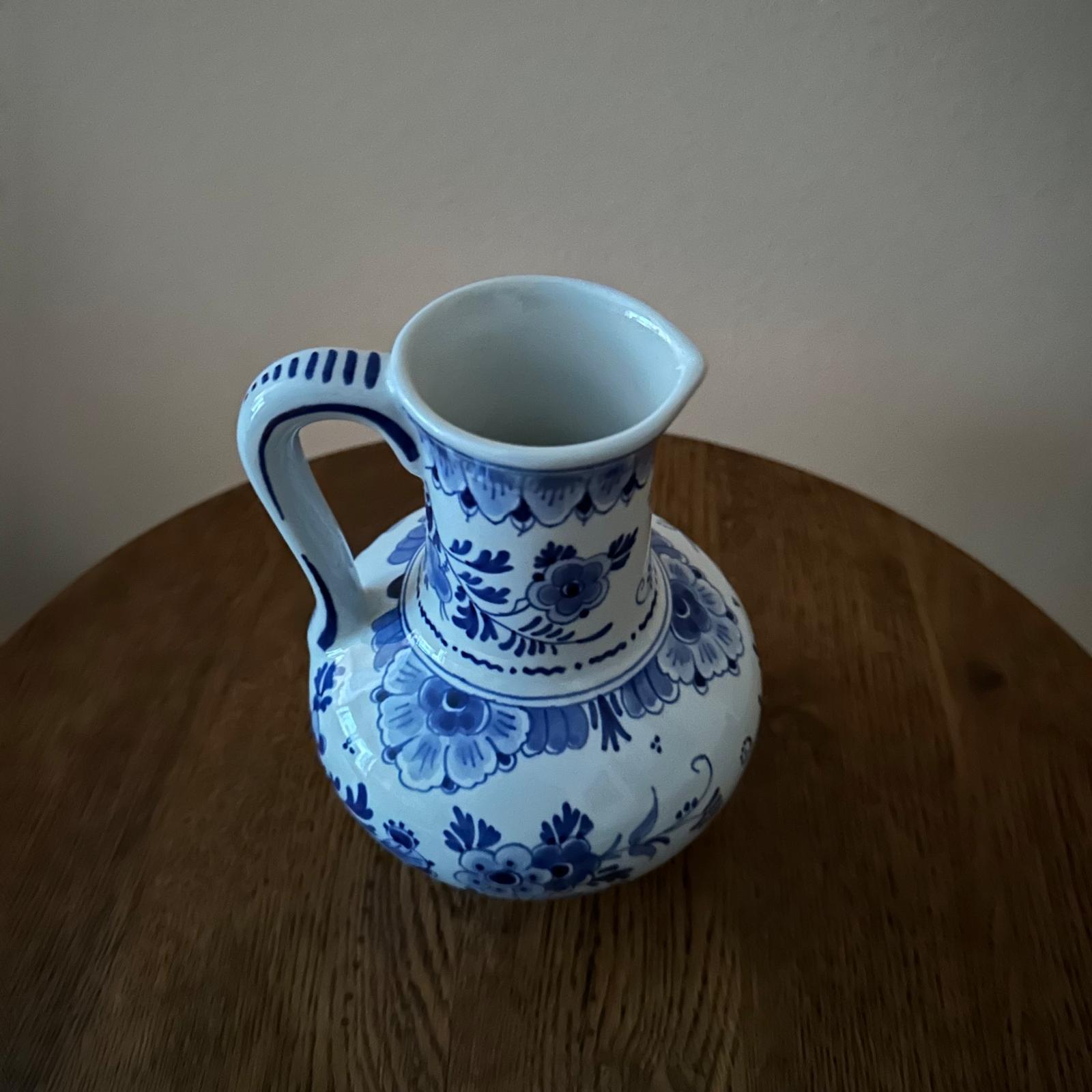 Blue and white floral-patterned ceramic pitcher on a wooden surface with a plain background