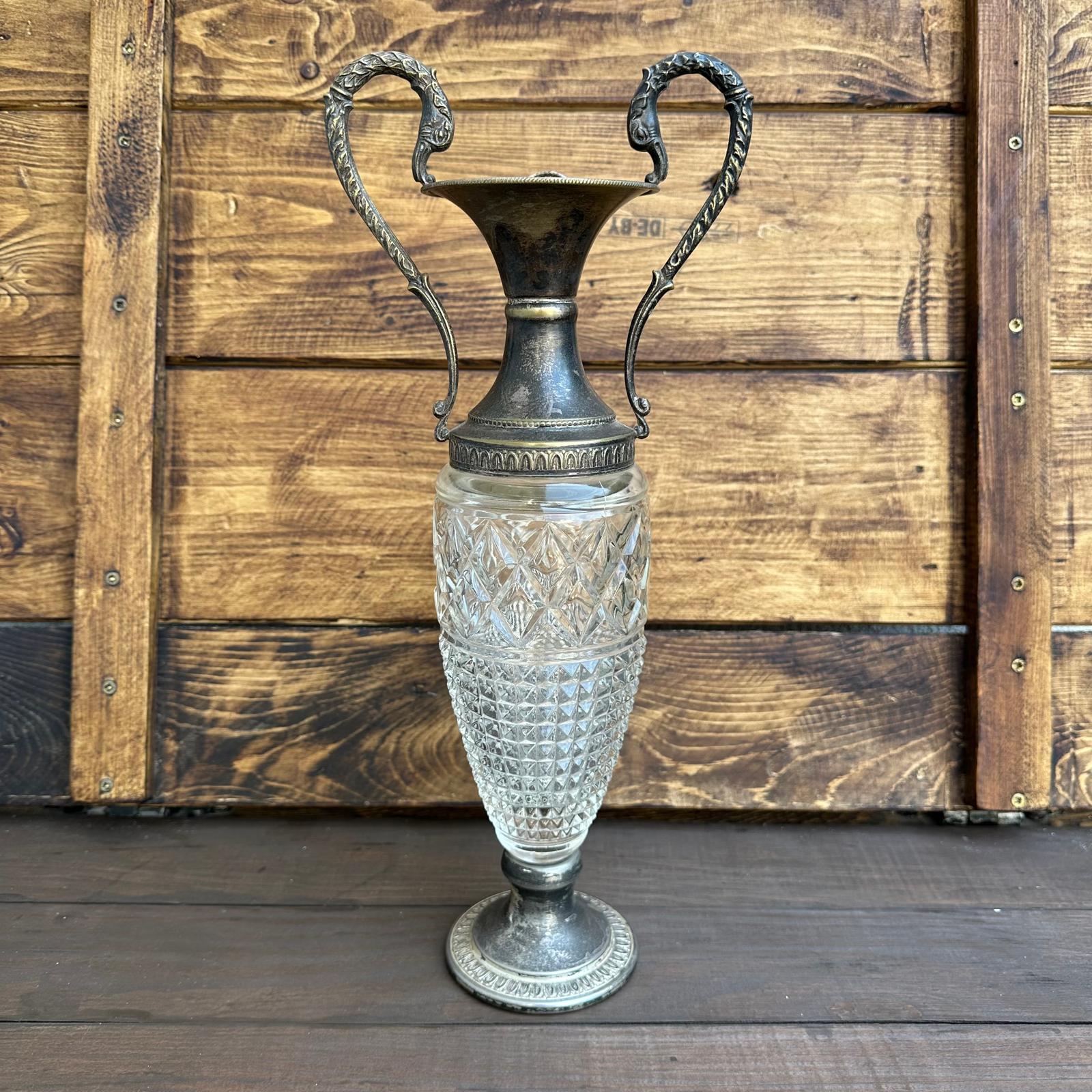 Decorative vase with crystal body and metal top against a wooden background