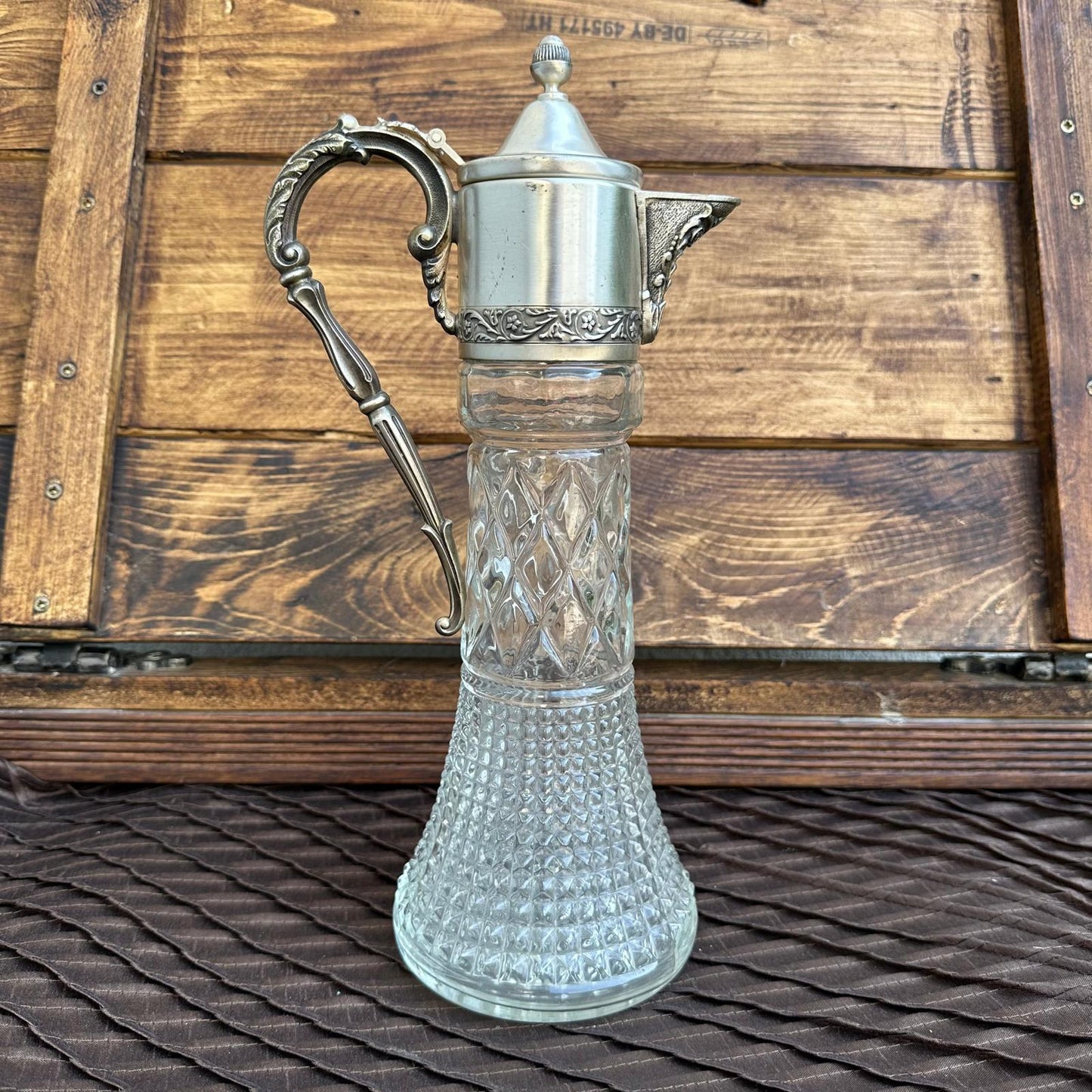 Vintage glass carafe with silver metal handle and lid on a wooden background