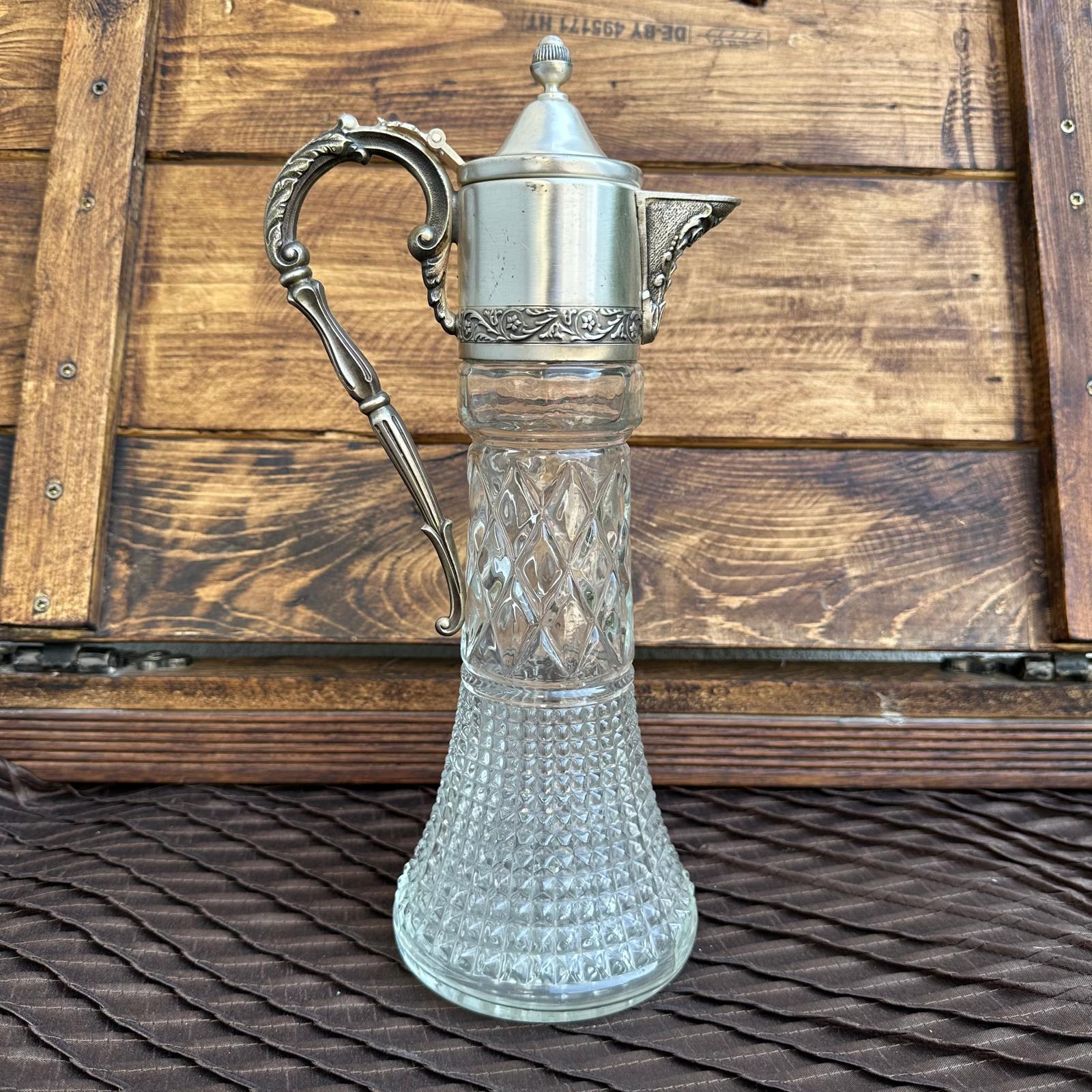 Vintage glass carafe with silver metal handle and lid on a wooden background