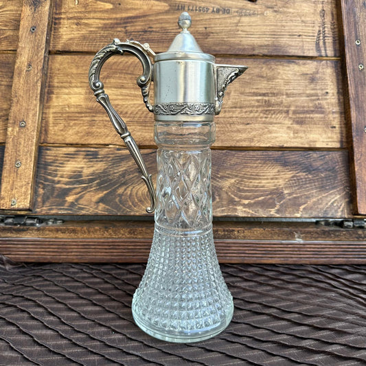 Vintage glass carafe with silver metal handle and lid on a wooden background