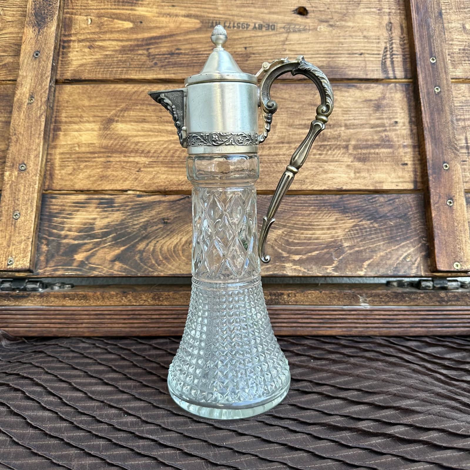 Clear glass carafe with silver metal handle and spout against a wooden background