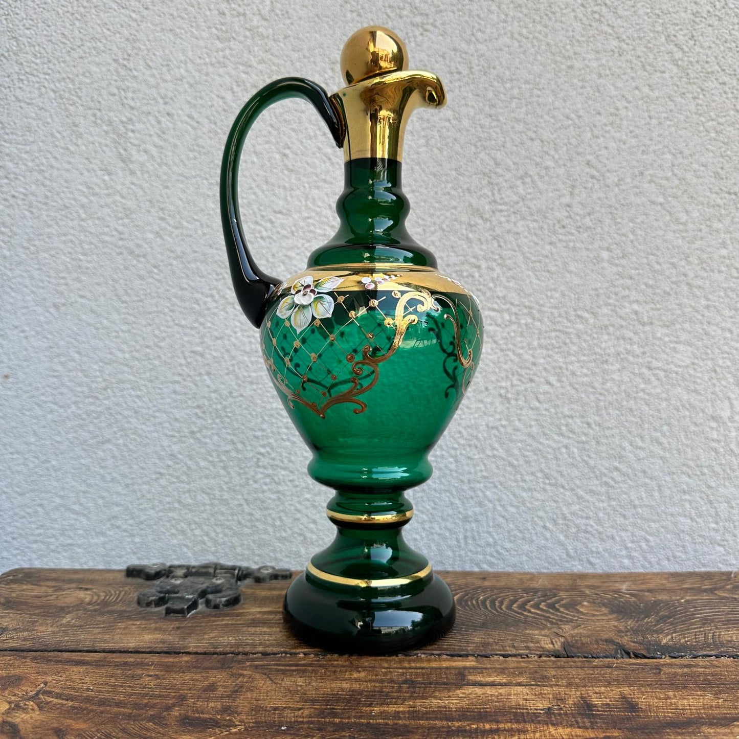 Green ceramic ewer with gold accents on a wooden surface