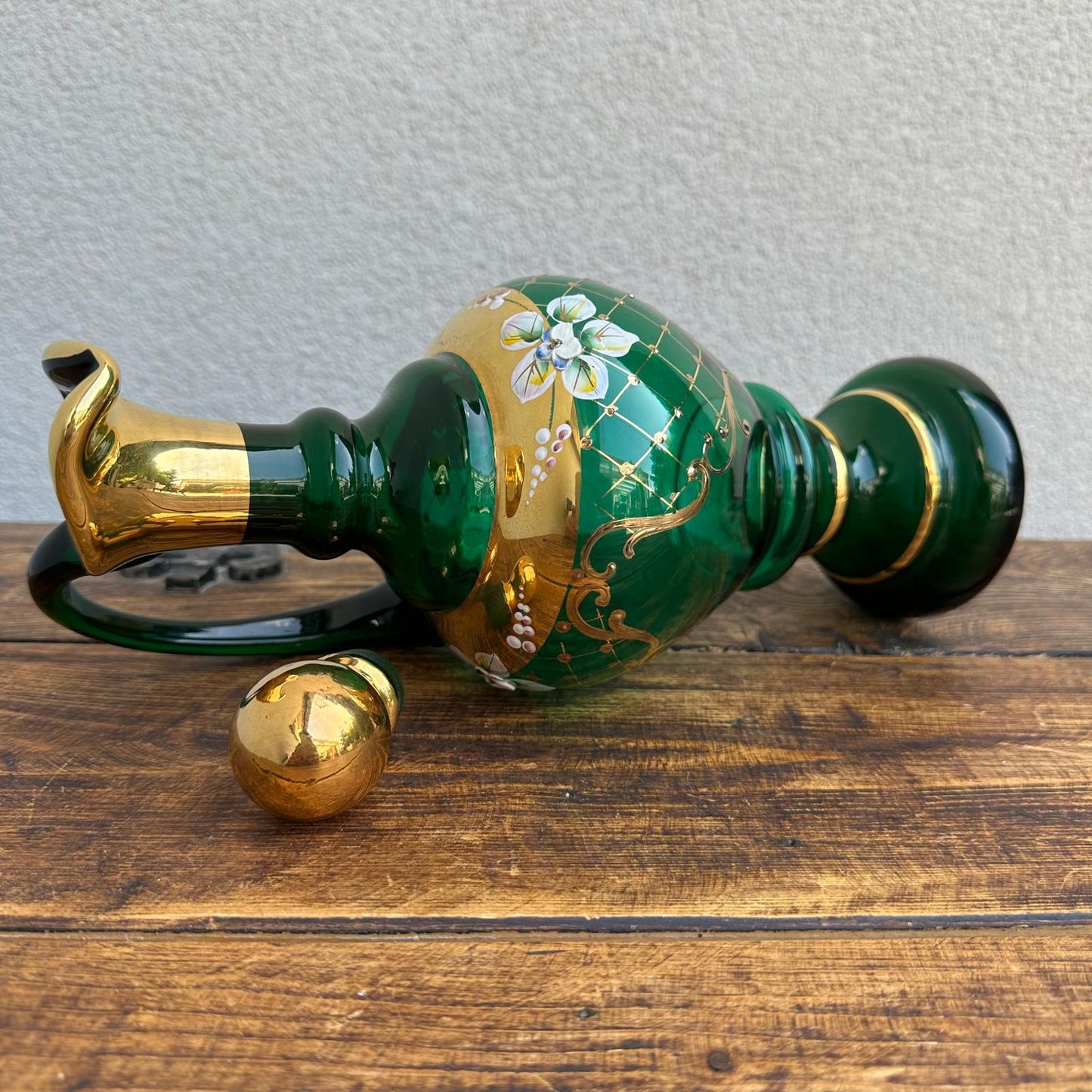 Decorative green and gold bottle on a wooden surface with a neutral background