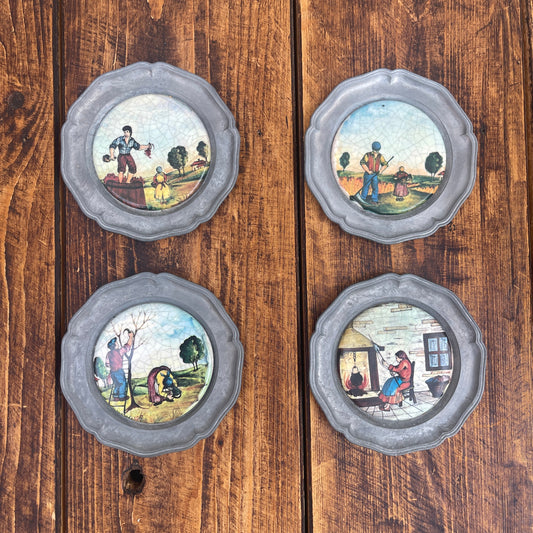 Four decorative plates with scenes of people in various activities on a wooden surface.