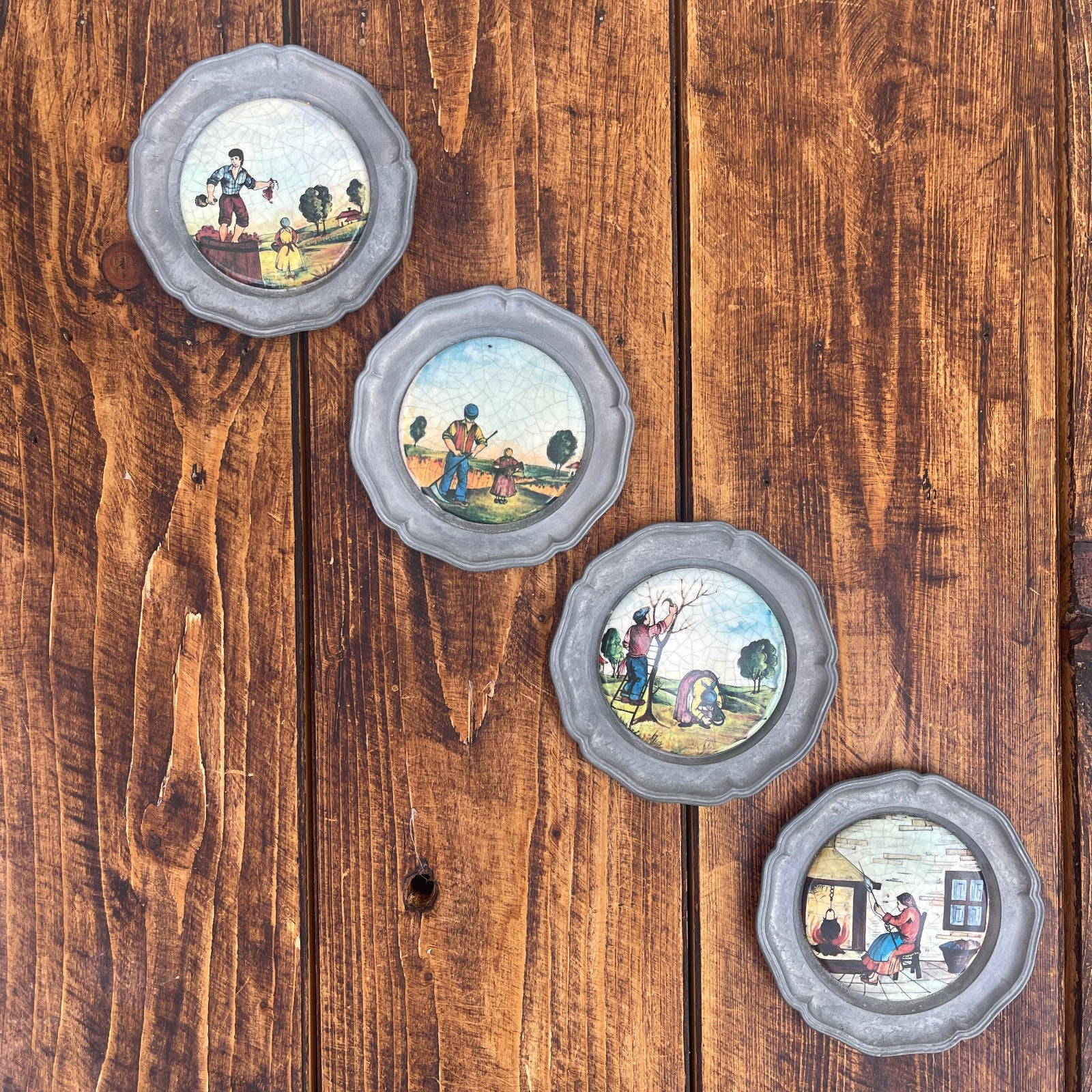 Set of four decorative plates with scenic illustrations on a wooden surface