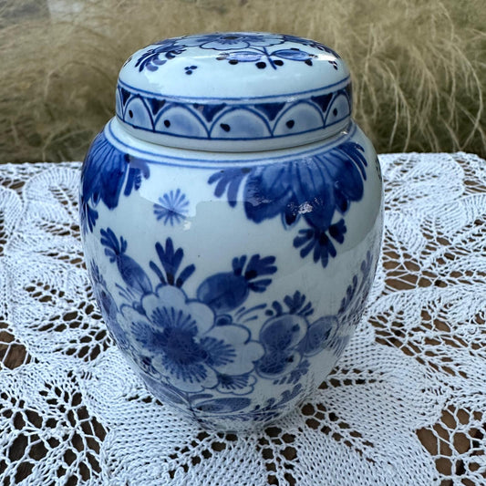 Blue and white floral-patterned ceramic jar on a lace tablecloth with blurred grass background