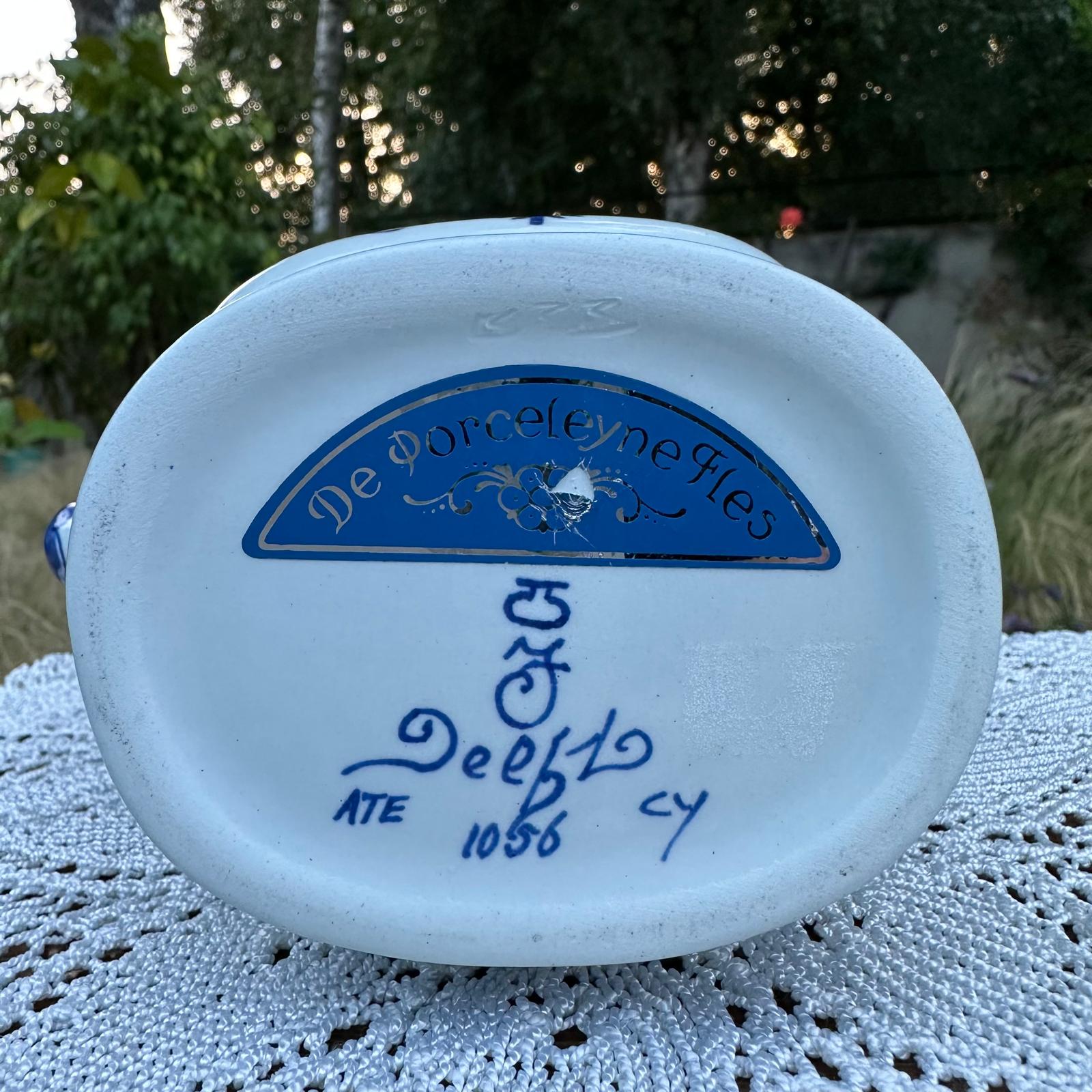 White ceramic item with blue text and logo on a textured surface with greenery in the background