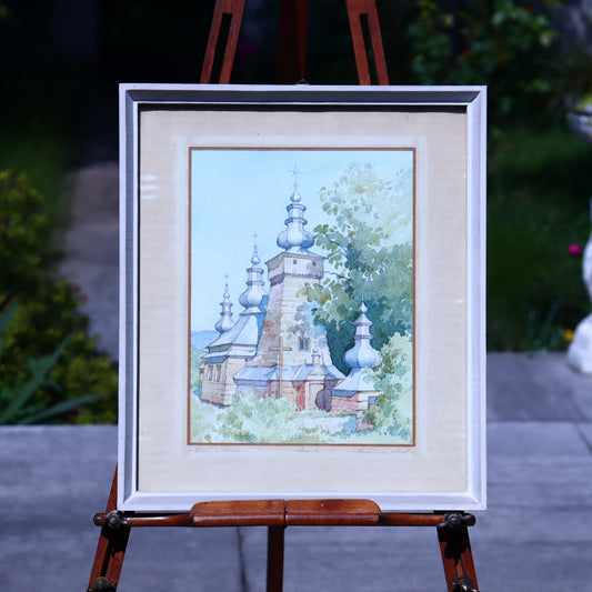 Framed painting of a church with trees on an easel outdoors