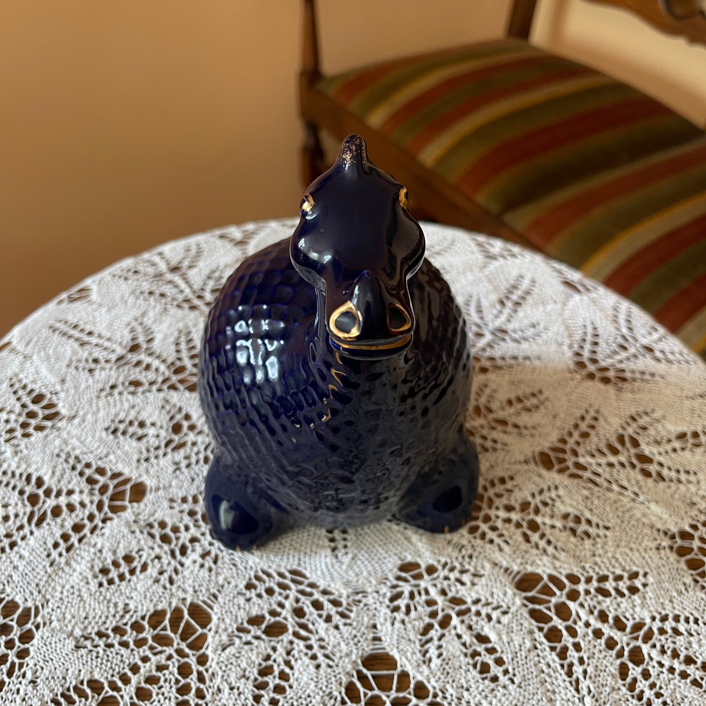 Blue ceramic cat figurine on a lace tablecloth with a striped cushion in the background