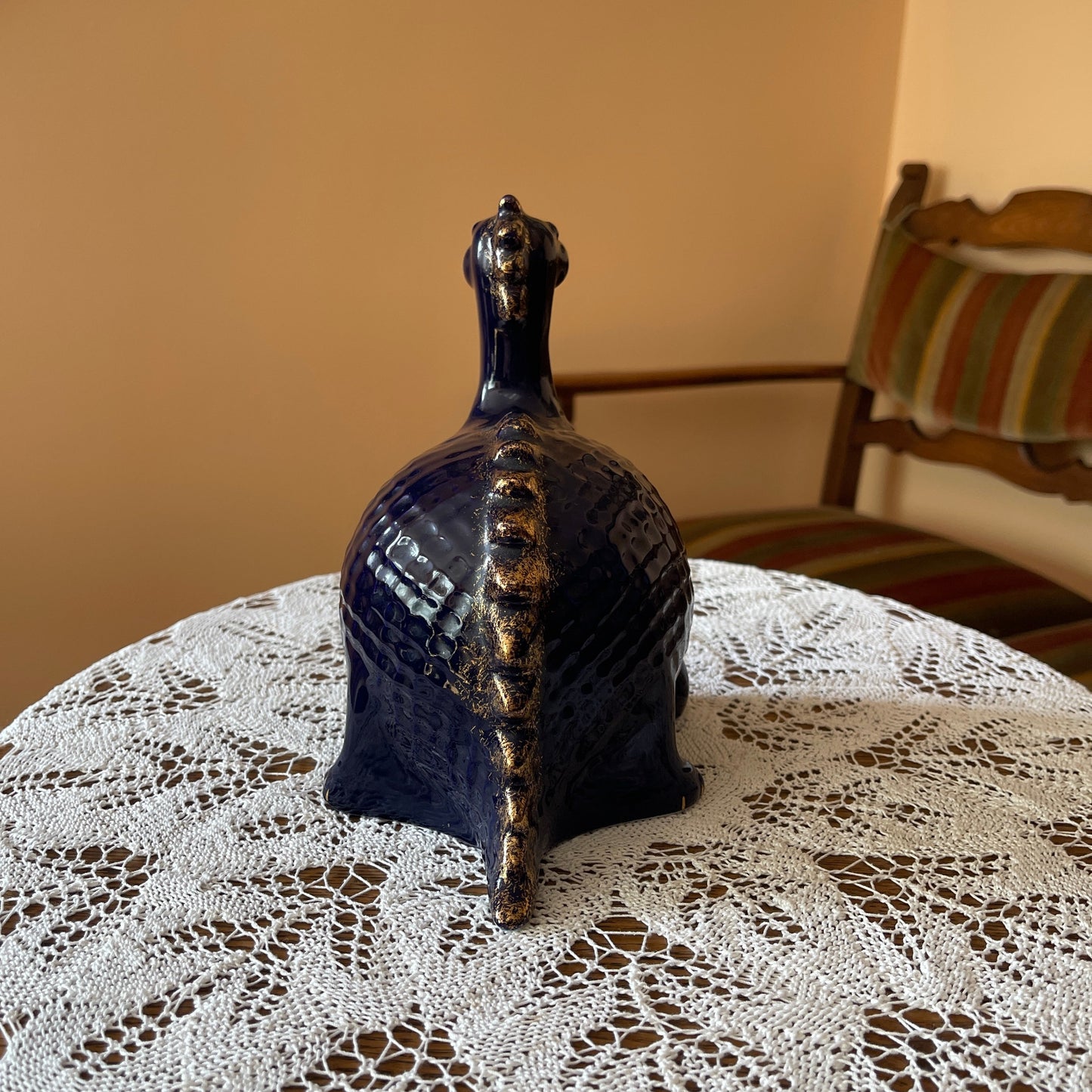 Decorative blue ceramic bird sculpture on a lace tablecloth with a chair in the background.