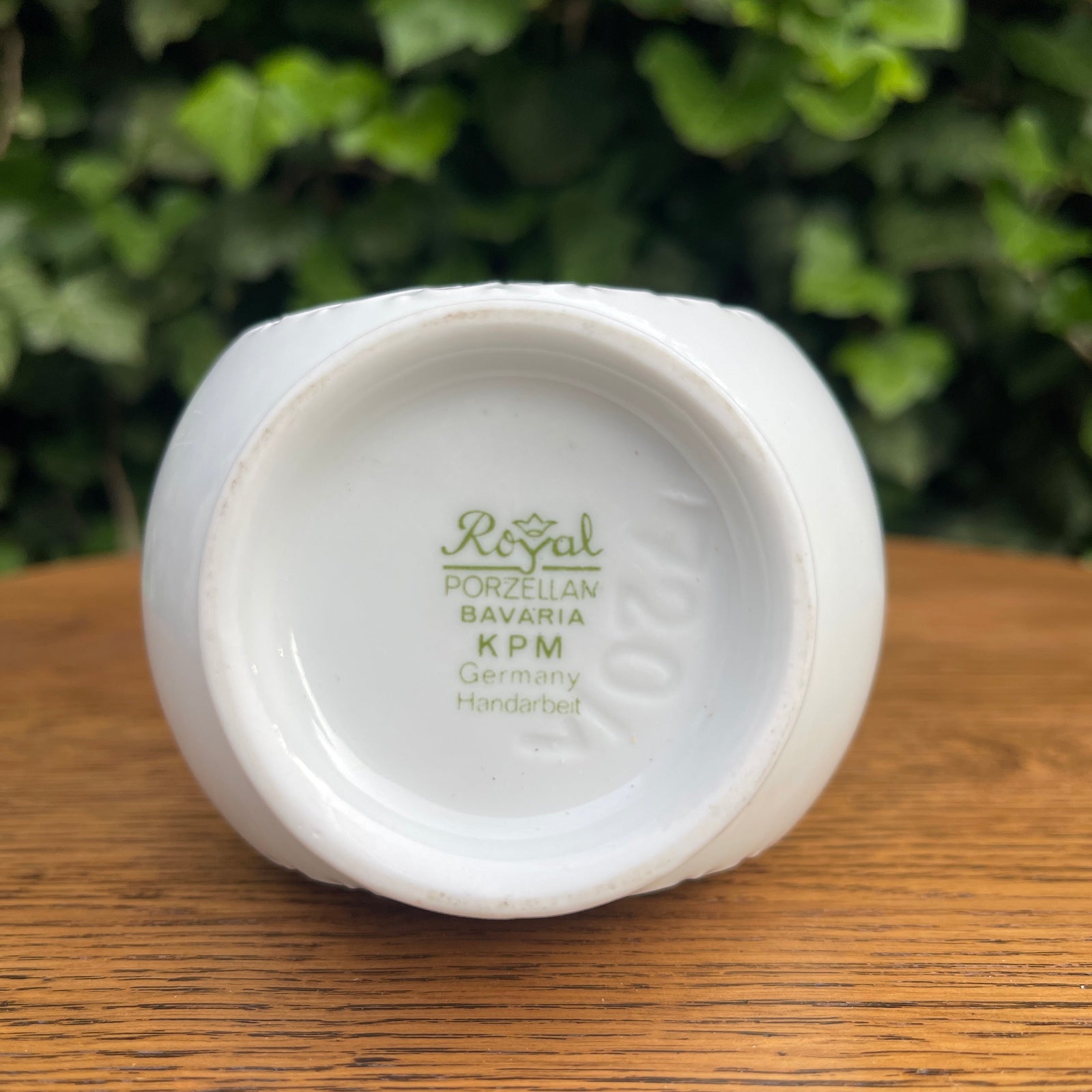 White ceramic item with 'Royal Porzellan Bavaria KPM Germany' branding on a wooden surface with greenery in the background.