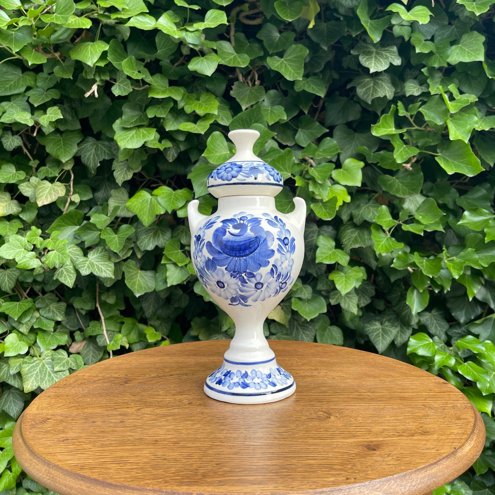 Blue and white floral-patterned urn on a wooden table with green foliage background