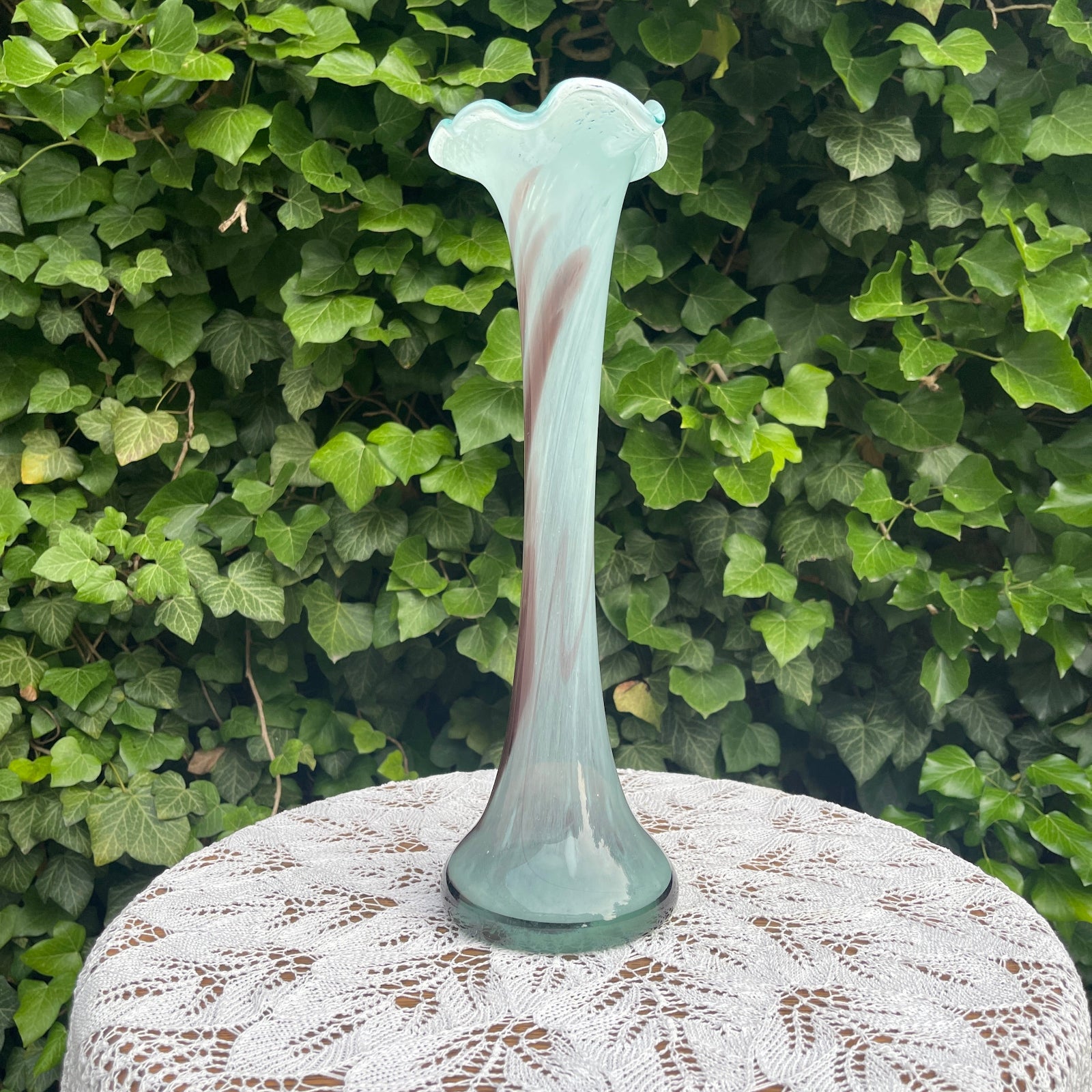 Glass vase with a floral design on a lace tablecloth against a green leafy background