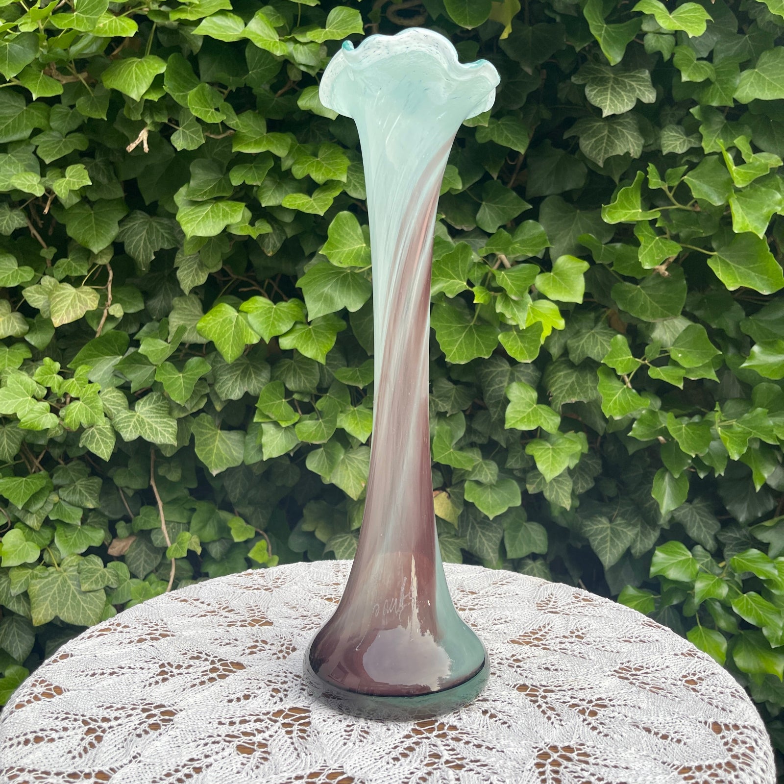 Decorative glass vase on a lace tablecloth with a green leafy background