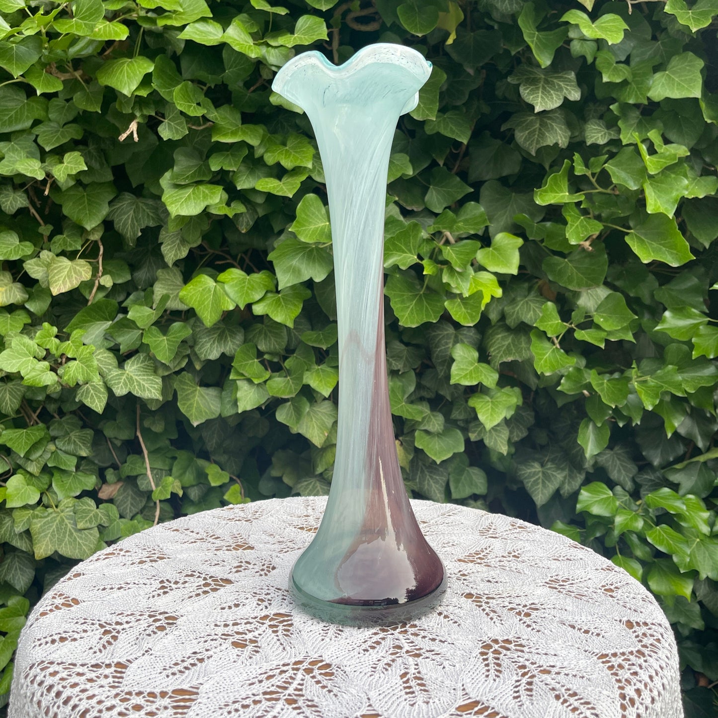 Glass vase on a lace tablecloth with green foliage background
