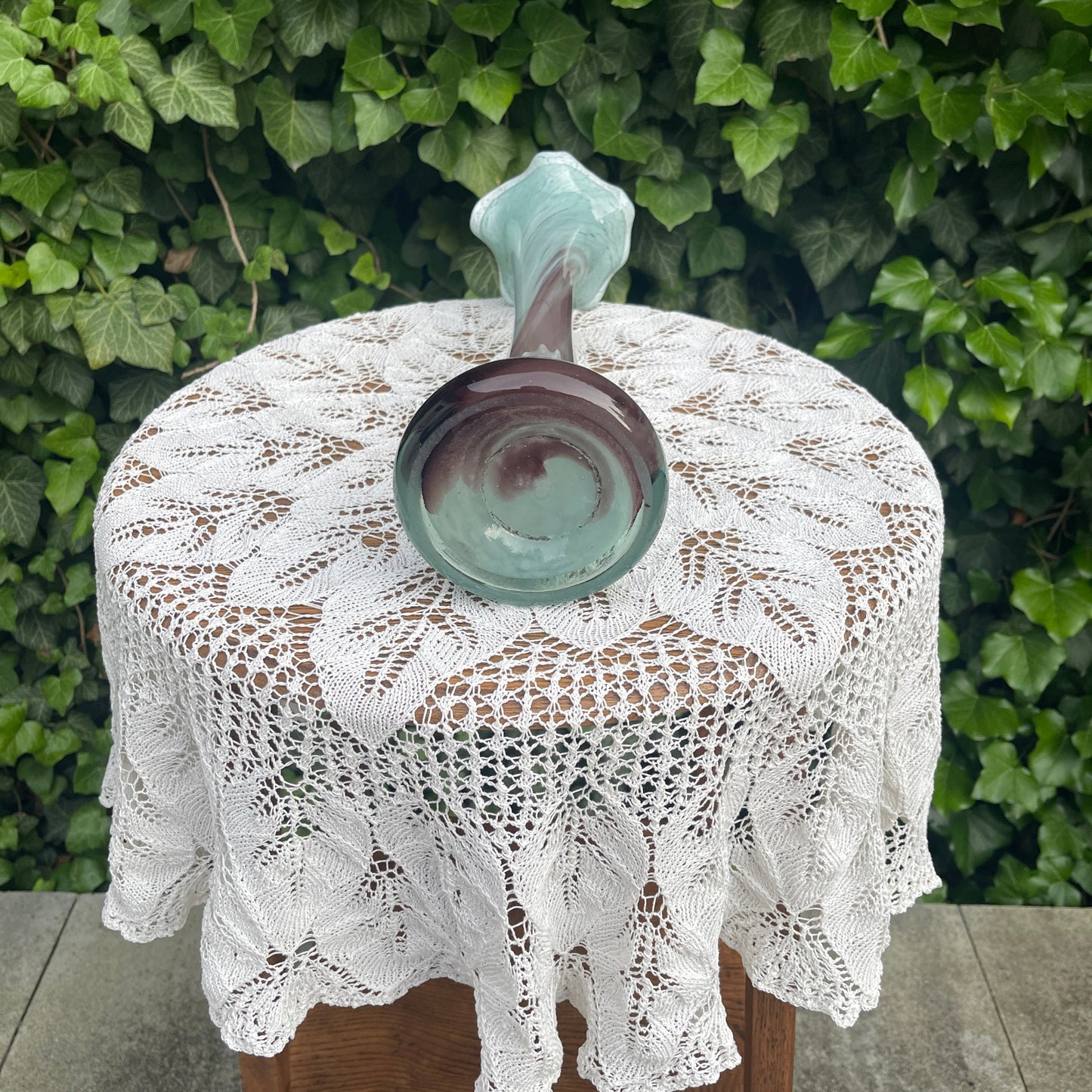 Lace tablecloth on a round table with a ceramic vase against a green leafy background