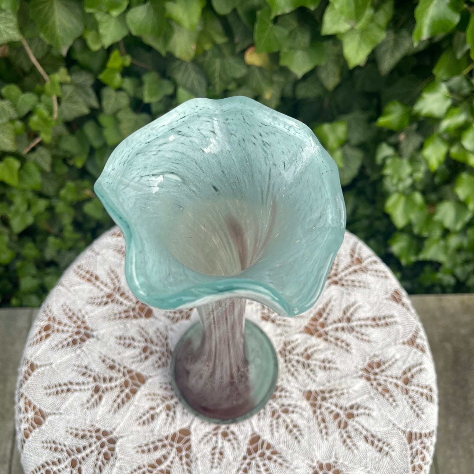 Turquoise glass vase on a textured surface with green foliage in the background